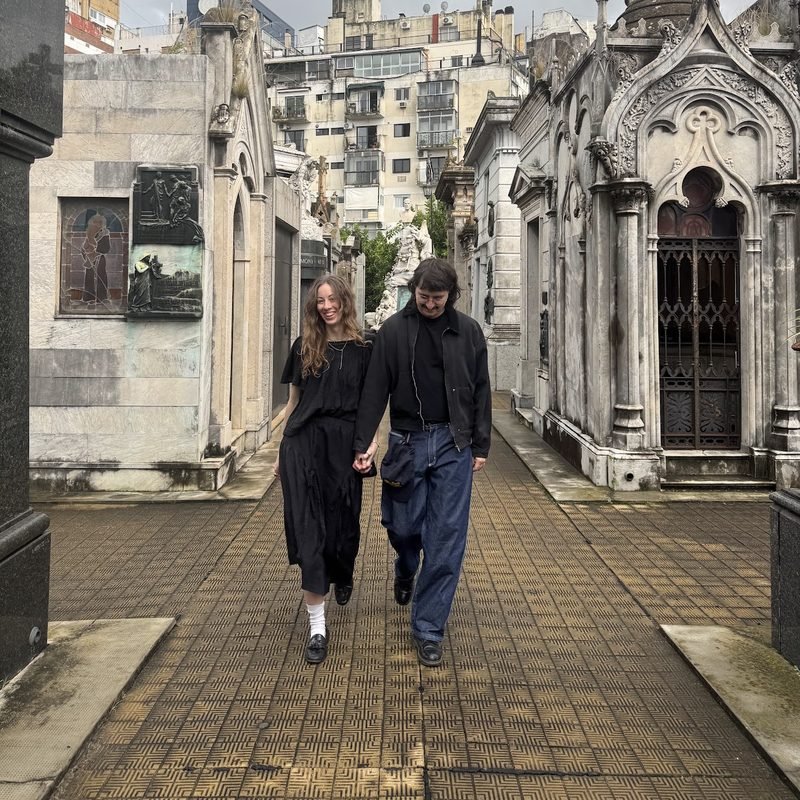 Simón and Tracy walking through a cemetery of ornate mausoleums